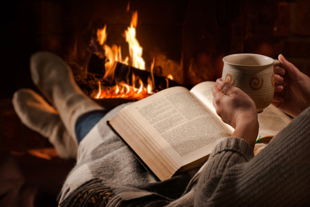 Woman reads book near fireplace