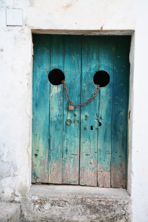 Photo of a wooden door on a stone building, shut with a chain and padlock. Used as photo prompt for flash fiction.