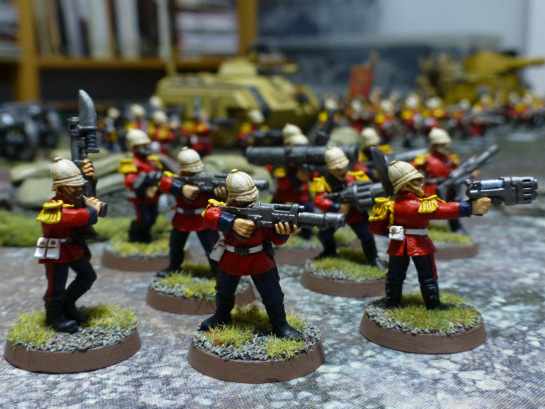 Soldiers with pith helmets and red uniform jackets aiming their weapons